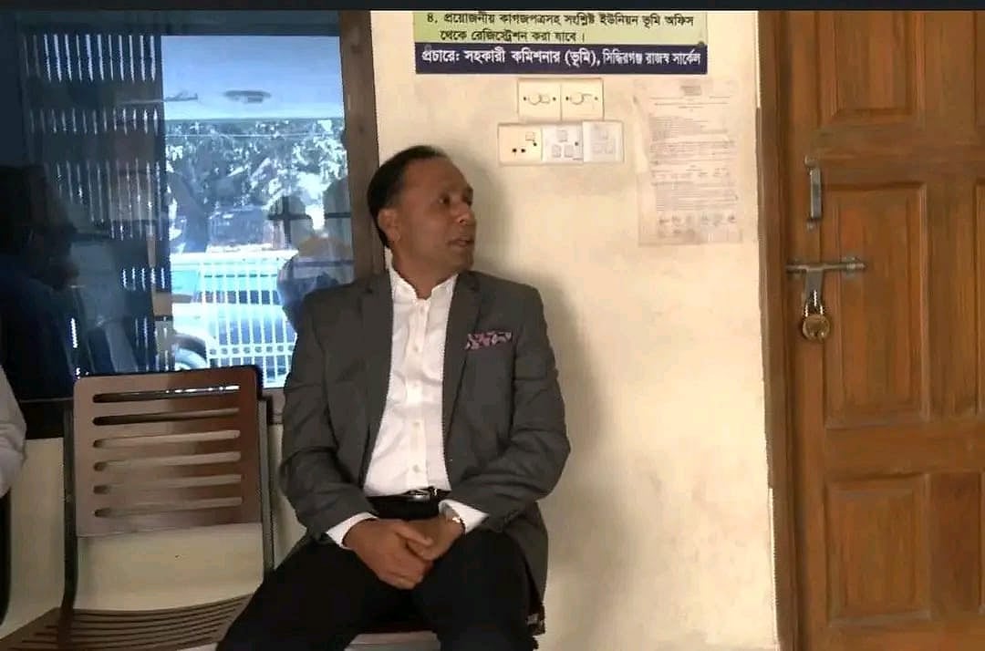 ভূমি কার্যালয়ের কর্মকর্তা কর্মচারীরা সময়মতো কর্মস্থলে না আসায় তাঁদের কক্ষগুলো তালাবদ্ধ। বাধ্য হয়ে কার্যালয়ের বারান্দায় বসে অপেক্ষা করছেন ভূমি প্রতিমন্ত্রী কায়সার কামাল। আজ বুধবার সকালে নারায়ণগঞ্জ সদর উপজেলার সিদ্ধিরগঞ্জ ইউনিয়ন ভূমি কার্যালয়ে