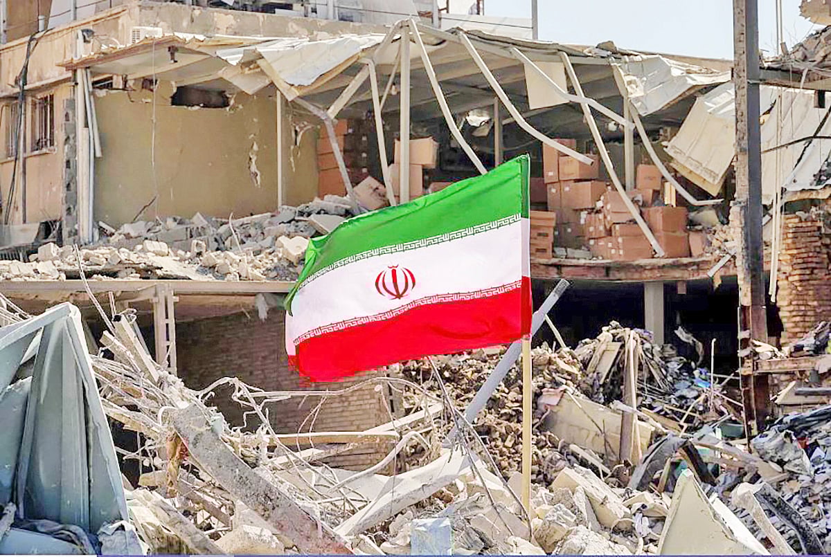 যুক্তরাষ্ট্র–ইসরায়েলের বোমা হামলায় বিধ্বস্ত ভবনের সামনে ইরানের পতাকা