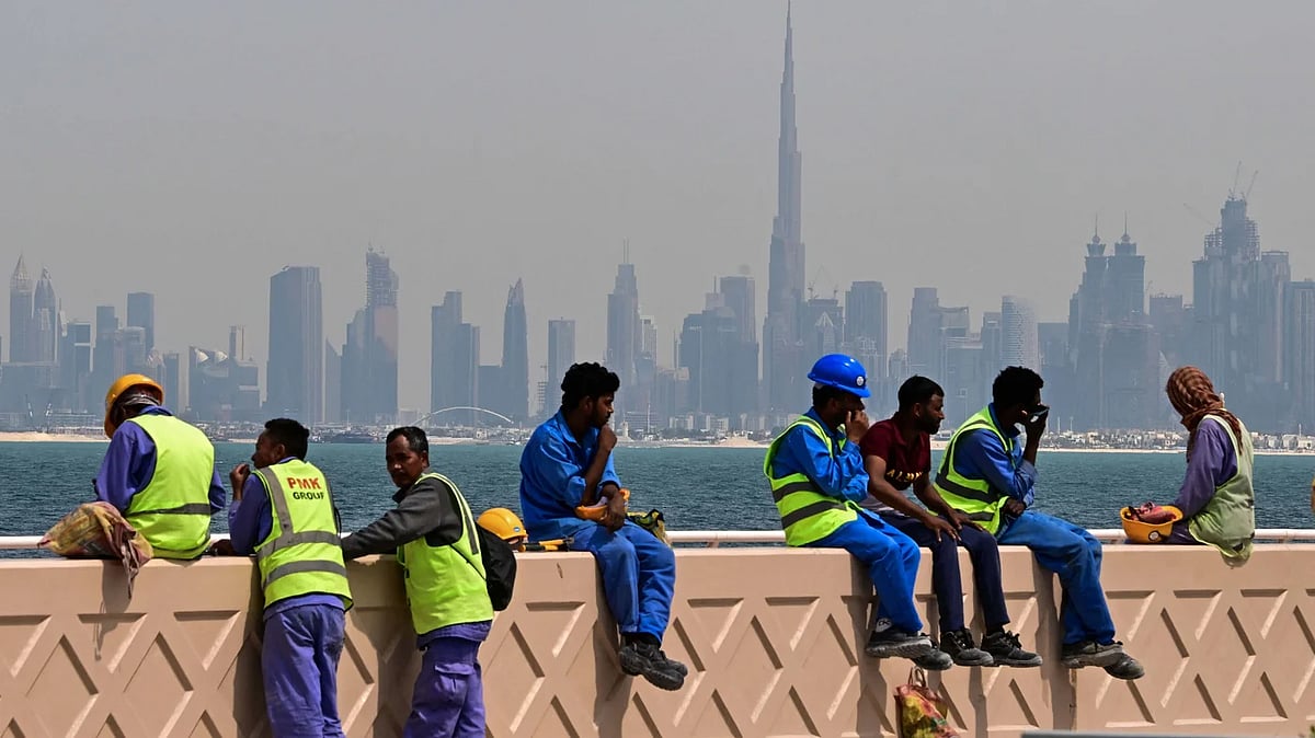 একটি দেয়ালের ওপর বসে বিশ্রাম নিচ্ছেন একদল অভিবাসী শ্রমিক। পেছনে সুউচ্চ দালানকোঠা। সংযুক্ত আরব আমিরাতের দুবাইয়ে, ১১ মার্চ ২০২৬