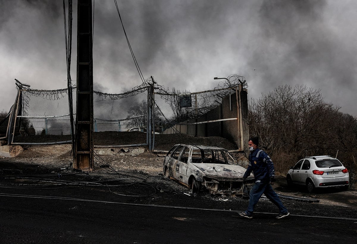 তেহরানের শাহরান জ্বালানি ডিপোতে হামলার পর উড়ছে ধোঁয়া, এর পাশেই একটি বিধ্বস্ত গাড়ির পাশ দিয়ে হেঁটে যাচ্ছেন এক ব্যক্তি। ৮ মার্চ ২০২৬