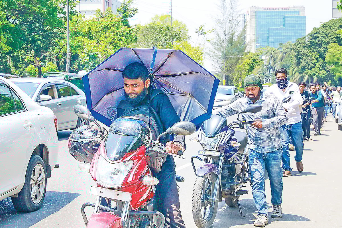প্রখর রোদে ঘণ্টার পর ঘণ্টা তেলের জন্য অপেক্ষা করছেন চালকেরা। ধীরে ধীরে লাইন এগোলে ছাতা মাথায় নিয়ে মোটরসাইকেল টেনে নিতে দেখা যায় এক চালককে। গতকাল বেলা একটার দিকে রাজধানীর বিজয় সরণি এলাকায় ট্রাস্ট ফিলিং স্টেশনের কাছে