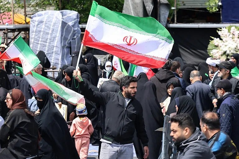 যুক্তরাষ্ট্র, ইসরায়েল ও ইরানের মধ্যে দুই সপ্তাহের যুদ্ধবিরতি চুক্তির পর তেহরানের রেভল্যুশন স্কয়ারে সমবেত মানুষের ভিড়ে ইরানের পতাকা নাড়ছেন এক ব্যক্তি। ৮ এপ্রিল ২০২৬  