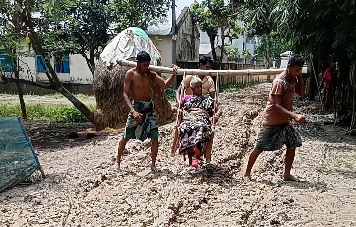 বাঁশে চেয়ার বেঁধে গ্রামের কাদা–পানিতে ভরা সড়ক দিয়ে মাকে হাসপাতালে নিয়ে যাচ্ছেন দুই ছেলে। বৃহস্পতিবার সকাল ১০টার দিকে দিনাজপুরের বিরামপুর উপজেলার সীমান্তবর্তী খিয়ারমামুদপুর গ্রামে