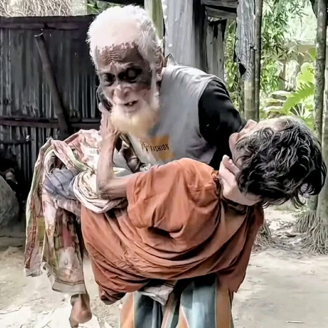 স্ত্রী নূরজাহান বেগমকে কোলে নিয়ে দাঁড়িয়ে আছেন সাজু শেখ। গত বুধবার বিকেলে শেরপুর সদর উপজেলার খুনুয়া চরপাড়া গ্রামে