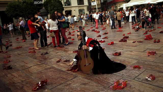A man dressed in a traditional dress of a university music group holds a guitar while in an art installation of 745 pairs of female red shoes. Photo: Reuters
