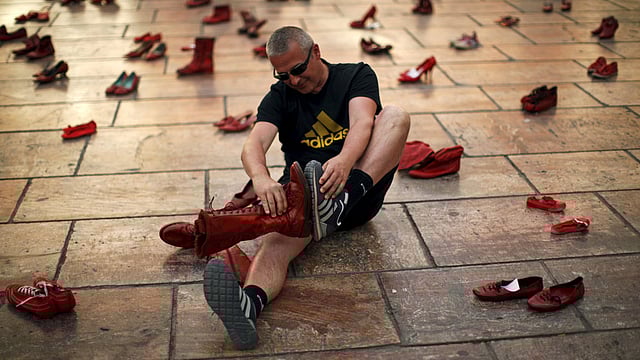 A man jokingly compares shoe sizes in an art installation of 745 pairs of female red shoes, put on display by Mexican visual artist Elina Chauvet to protest against gender violence and femicide. Photo: Reuters