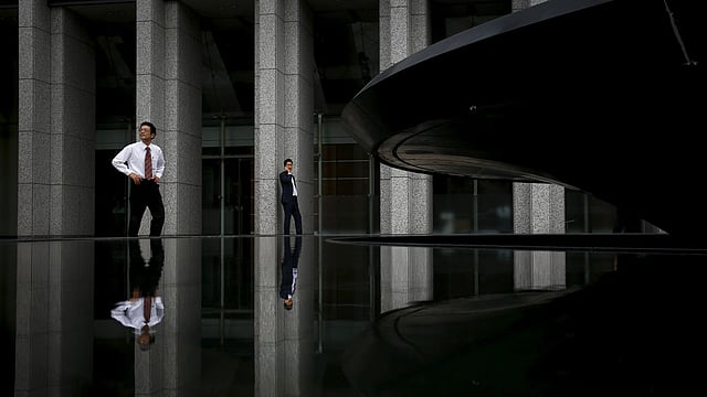 Businessmen are reflected in a fountain as they stand outside an office building in Tokyo, Japan August 14, 2015. Photo: Reuters