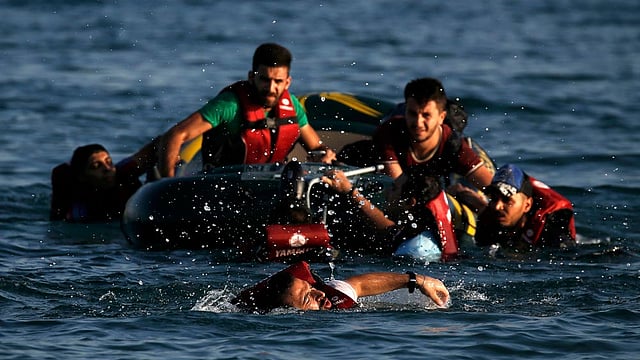 A Syrian refugee swims towards a beach as others are seen on a dinghy whose engine broke down a few hundred metres from the shore of the Greek island of Kos after crossing over from Turkey, August 17, 2015. Photo: Reuters