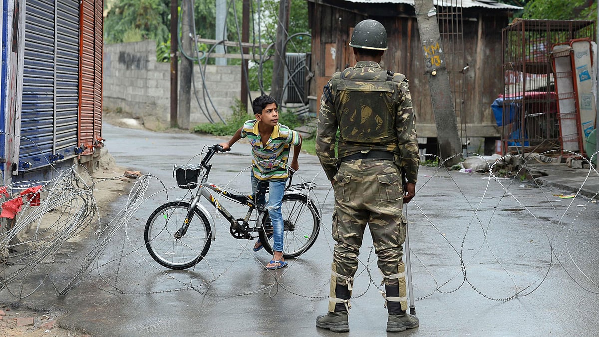 An Indian paramilitary trooper stands guard as a Kashmiri child looks out from behind a barbed wire cordon during a curfew in Srinagar on 27 August. Photo: AFP