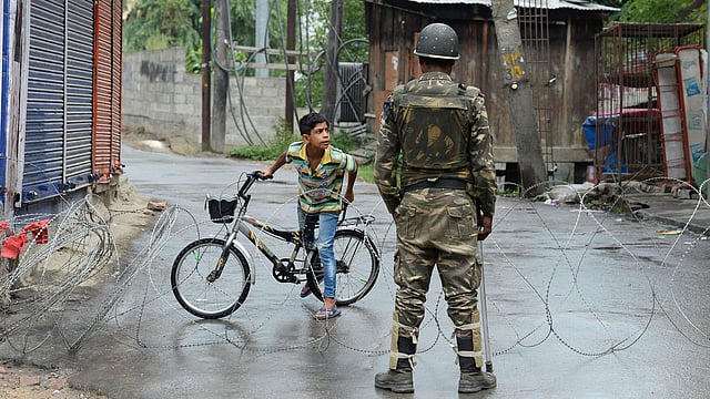 An Indian paramilitary trooper stands guard as a Kashmiri child looks out from behind a barbed wire cordon during a curfew in Srinagar on 27 August. Photo: AFP