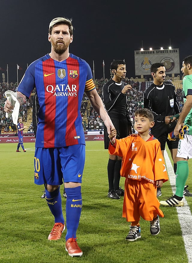 FC Barcelona Lionel Messi (L) holds the hands of Afghan boy Murtaza Ahmadi on the pitch before the start of a friendly football match against Saudi Arabia’s Al-Ahli FC. Photo: AFP