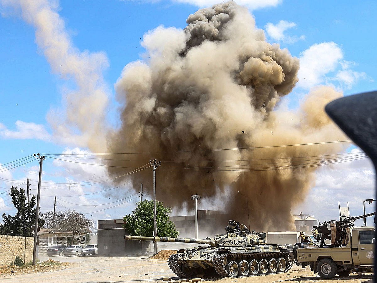 This picture taken on 12 April, 2019 shows a smoke plume rising from an air strike behind a tank and technicals (pickup trucks mounted with turrets) belonging to forces loyal to Libya`s Government of National Accord (GNA), during clashes in the suburb of Wadi Rabie about 30 kilometres south of the capital Tripoli. Photo: AFP