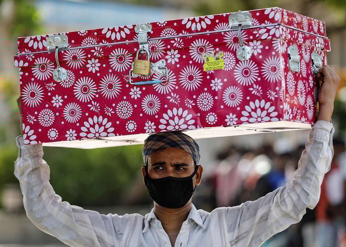 A migrant worker carries a luggage trunk on his head as he waits for transport to reach a railway station to board a train to his home state of Bihar, during an extended lockdown to slow the spreading of the coronavirus disease (COVID-19), in Ahmedabad, India on 23 May.