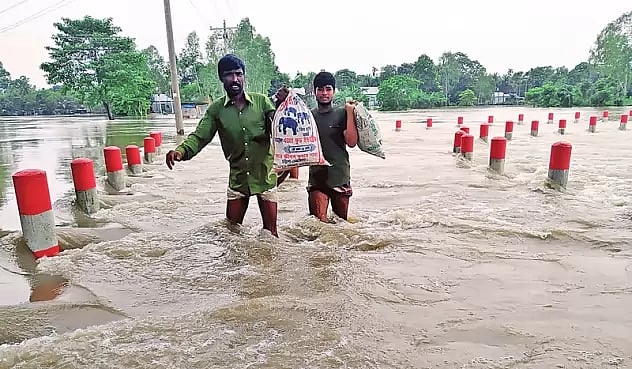 Two men carry sacks along a flooded road in Jamalpur on 30 June 2020.