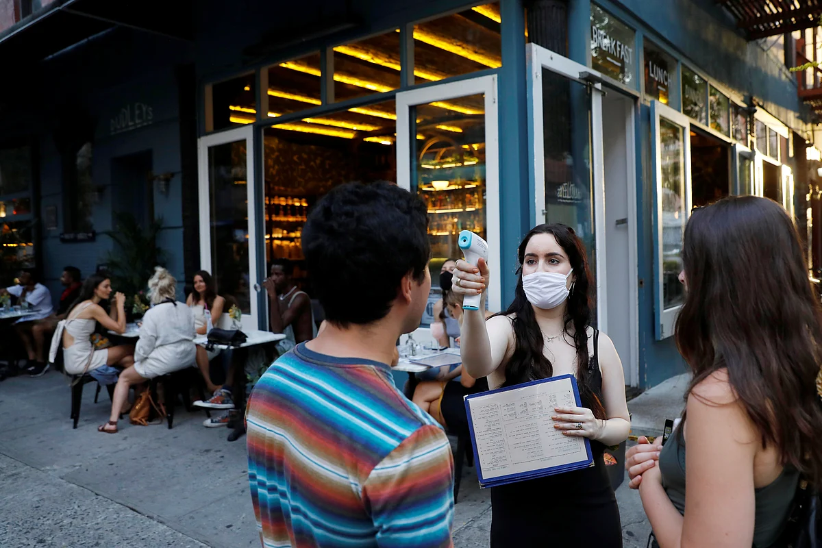 A waitress takes the temperature of customers as they arrive to eat at Dudley's as restaurants in New York City, US on 27 June.