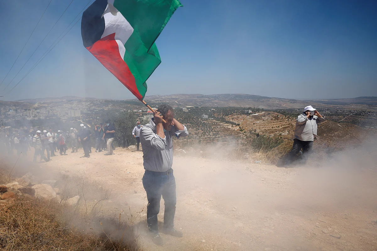 A Palestinian demonstrator reacts to a sound grenade fired by Israeli forces during a protest against Jewish settlements and Israel's planned annexation of parts of the Israeli-occupied West Bank, in the Palestinian town of Asira ash-Shamaliya, 17 July 2020.