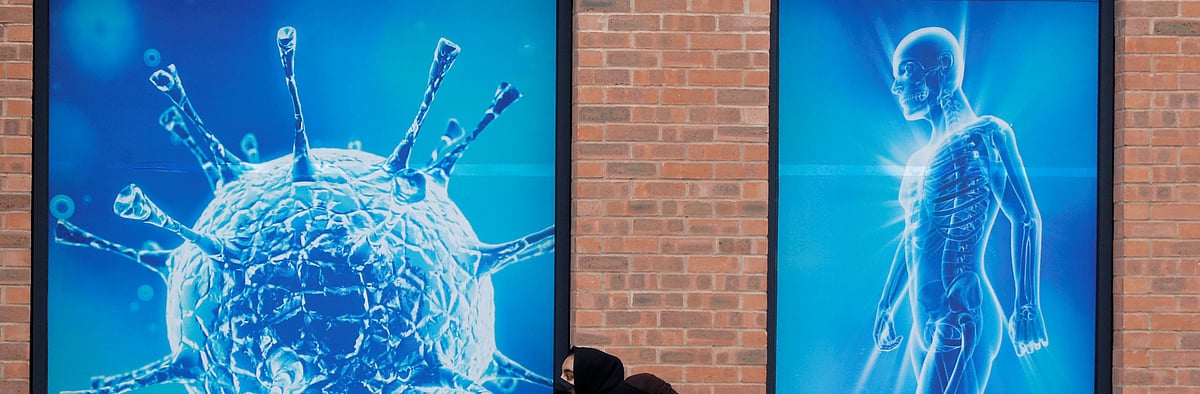 People walk past an illustration of a virus outside a regional science centre, as the city and surrounding areas face local restrictions in an effort to avoid a local lockdown being forced upon the region, amid the coronavirus disease (COVID-19) outbreak, in Oldham, Britain 3 August 2020 REUTERS/Phil Noble