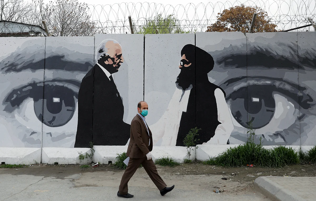 An Afghan man wearing a protective face mask walks past a wall painted with photo of Zalmay Khalilzad, US envoy for peace in Afghanistan, and Mullah Abdul Ghani Baradar, the leader of the Taliban delegation, in Kabul.