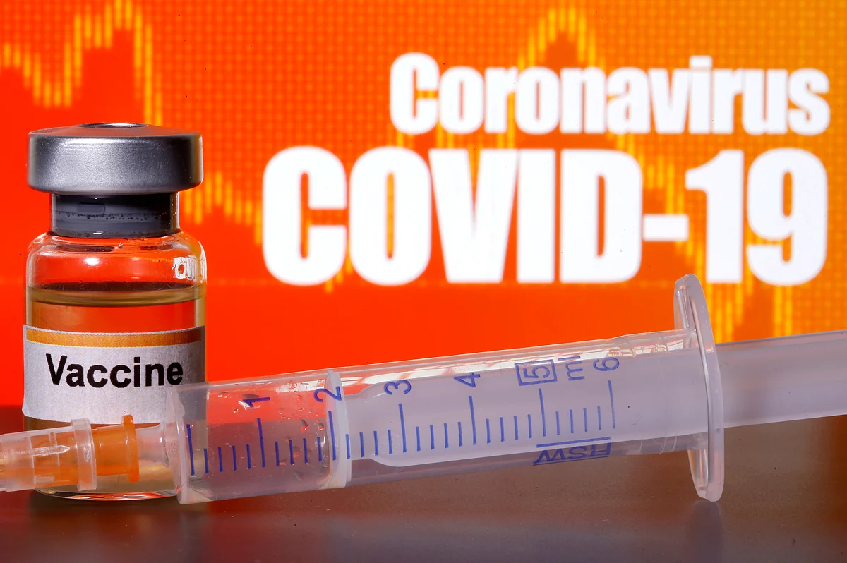 A small bottle labeled with a 'Vaccine' sticker stands near a medical syringe in front of displayed 'Coronavirus COVID-19' words in this illustration taken 10 April 2020.