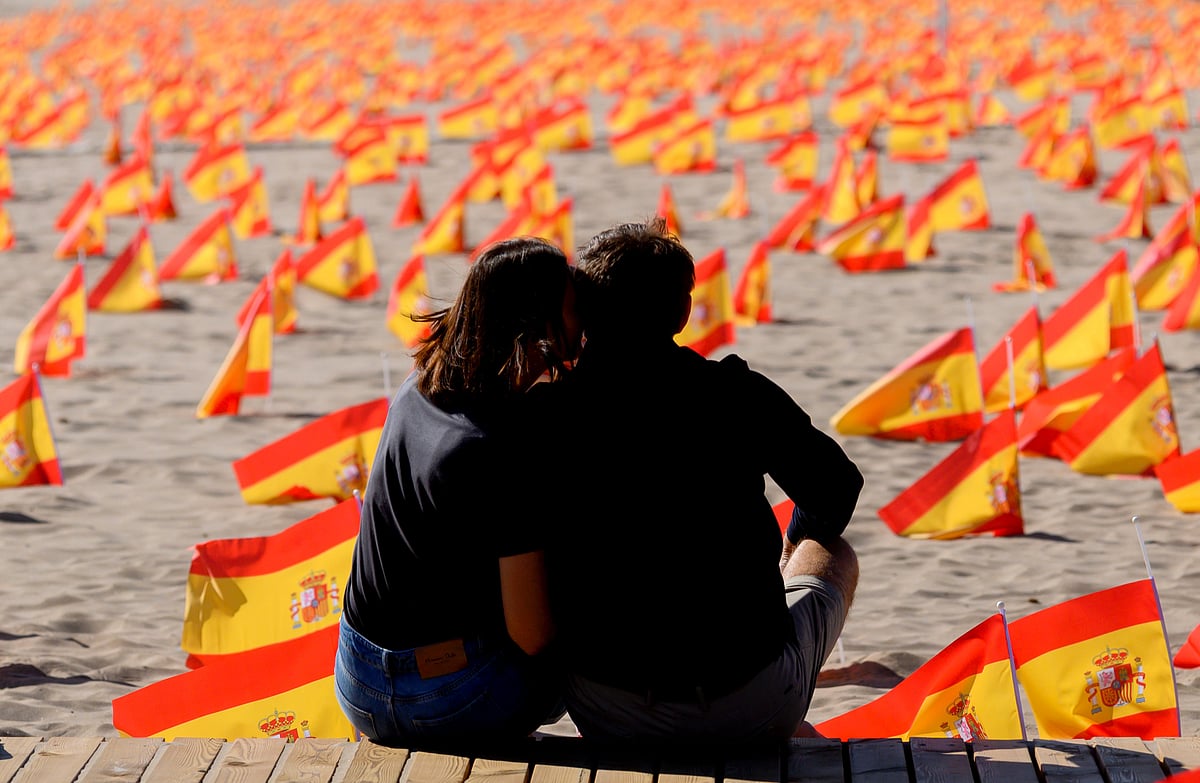 In this file photo taken on 4 October 2020 a couple sit next to thousands of Spanish flags, representing the Spanish victims of COVID-19, on Patacona beach in Valencia. Spain surpassed one million virus cases on October 21, 2020 according to health ministry figures AFP