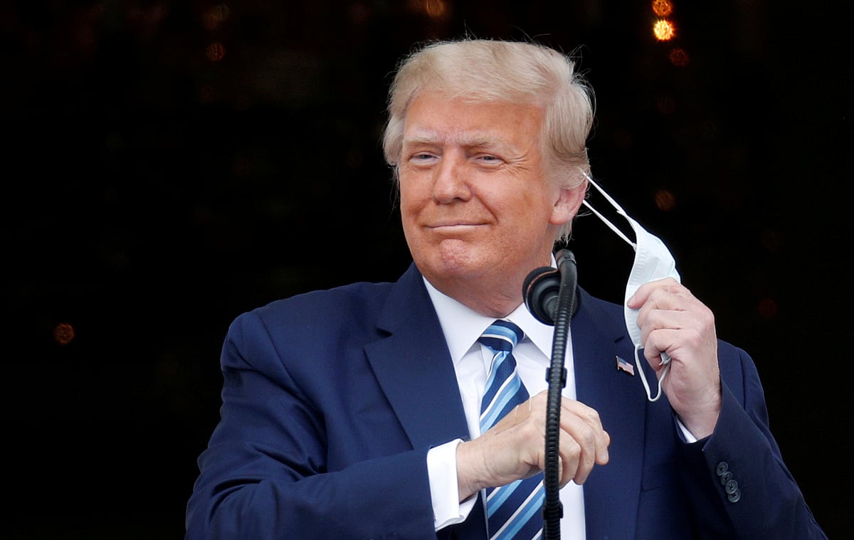 US president Donald Trump, with bandages seen on his hand, takes off his face mask as he comes out on a White House balcony to speak to supporters gathered on the South Lawn for a campaign rally that the White House is calling a "peaceful protest" in Washington, US, on 10 October 2020