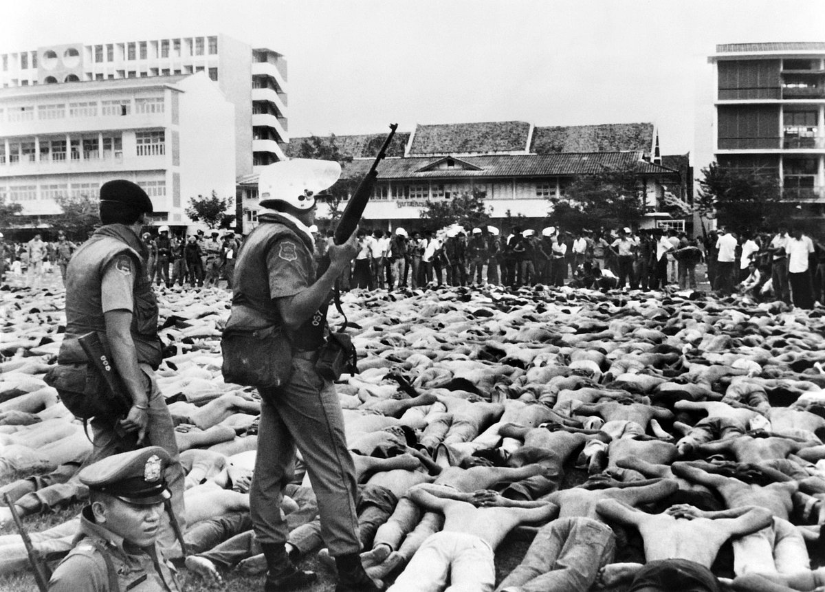 In this file photo taken on 6 October 1976, shirtless students lie facedown on the ground, with their hands behind their heads, as police stand guard on the Thammasat University campus in Bangkok, when students protesting the return of a military dictator were shot, beaten to death and lynched by state forces and royalist mobs.