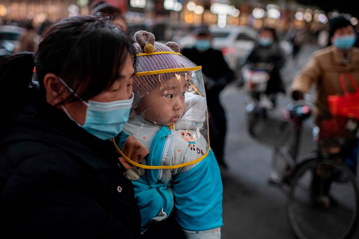 A woman wearing a face mask holds a baby that wears a protective shield during rush hour on a street outside of a shopping mall complex in Wuhan on 13 January 2021. A team of WHO experts will land directly in Wuhan on 14 January 2021, China's foreign ministry said, starting their long-delayed probe into Covid-19 at the virus epicentre.
