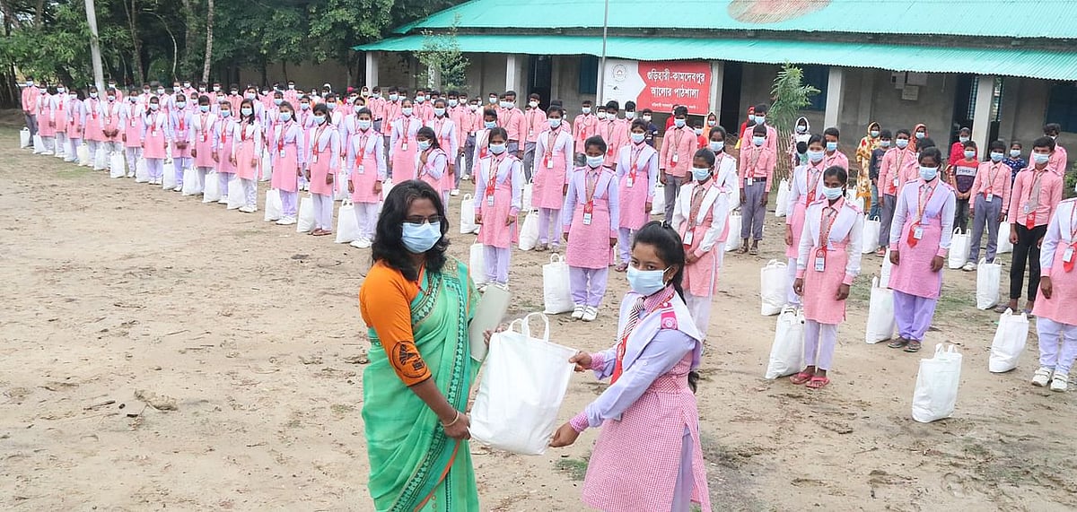 Prothom Alo Trust, with support from Summit Group, distributed Eid gifts among the students of Gurihari-Kamdebpur Alor Pathshala. Niatmatpur UNO Joya Maria Pereira hands out the gifts to the students on Saturday at the school grounds.