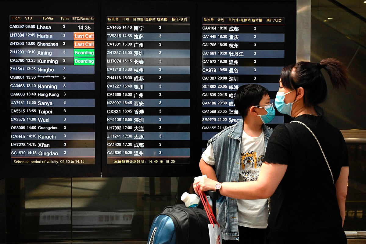 Travellers wearing face masks wait in front of a departures board at Beijing’s Capital international airport on 10 August 2021