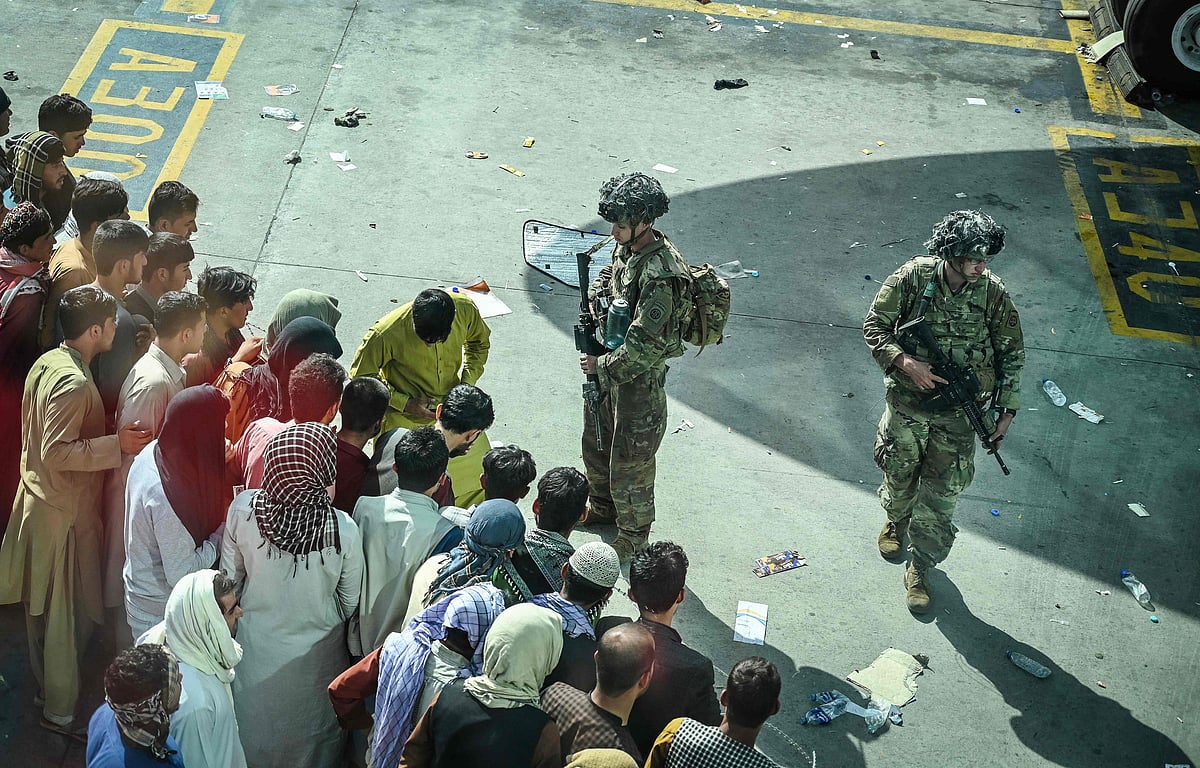 US soldiers stand guard as Afghan people wait at the Kabul airport in Kabul on 16 August 2021, after a stunningly swift end to Afghanistan's 20-year war, as thousands of people mobbed the city's airport trying to flee the group's feared hardline brand of Islamist rule.