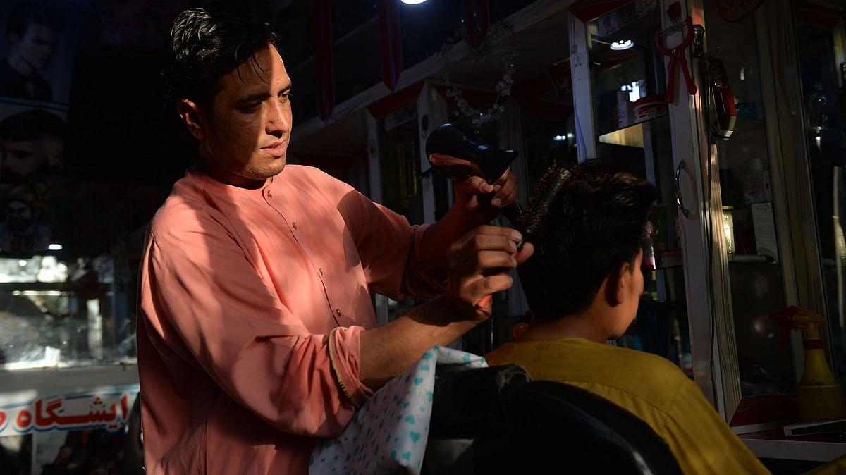 In this picture taken on 19 September 2021, 24-year-old Nader Shah (L) attends a customer at his barbershop in Herat