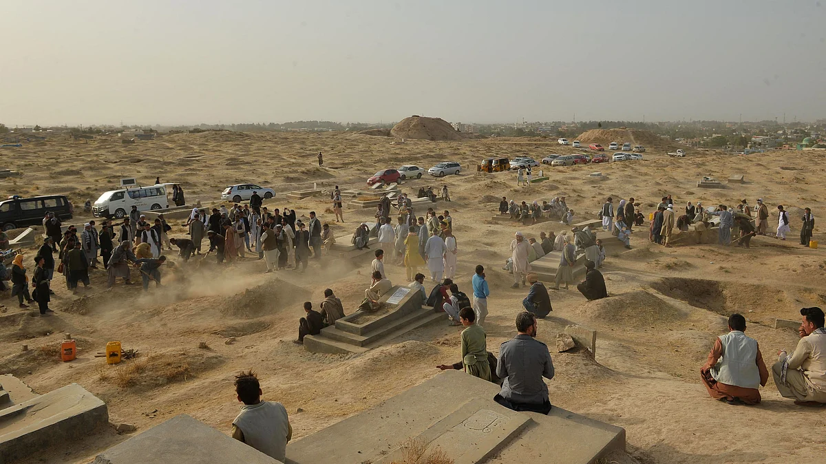 Relatives and friends stand next to graves of victims of yesterday's suicide bomb attack on worshippers at a Shiite mosque, in which at least 55 people died, at a graveyard in Kunduz on 9 October 2021