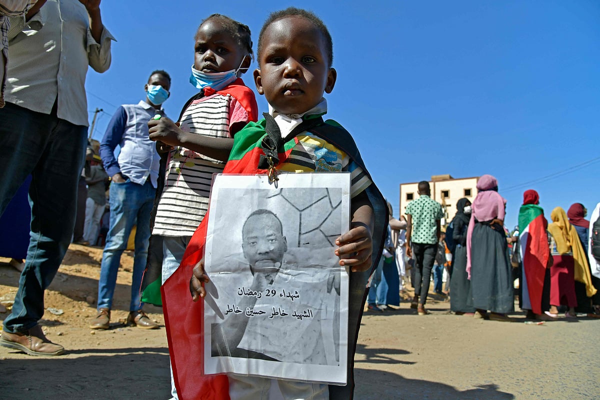 A Sudanese boy draped in the national flag lifts a portrait of a slain protester during a demonstration calling for a return to civilian rule in 40th street in the capital's twin city of Omdurman, on 21 November, 2021