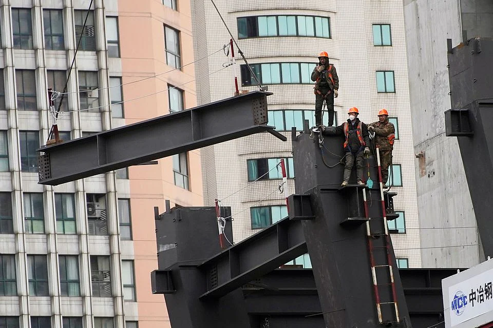 Workers watch as a crane lifts a structure at a construction site in Shanghai, China.