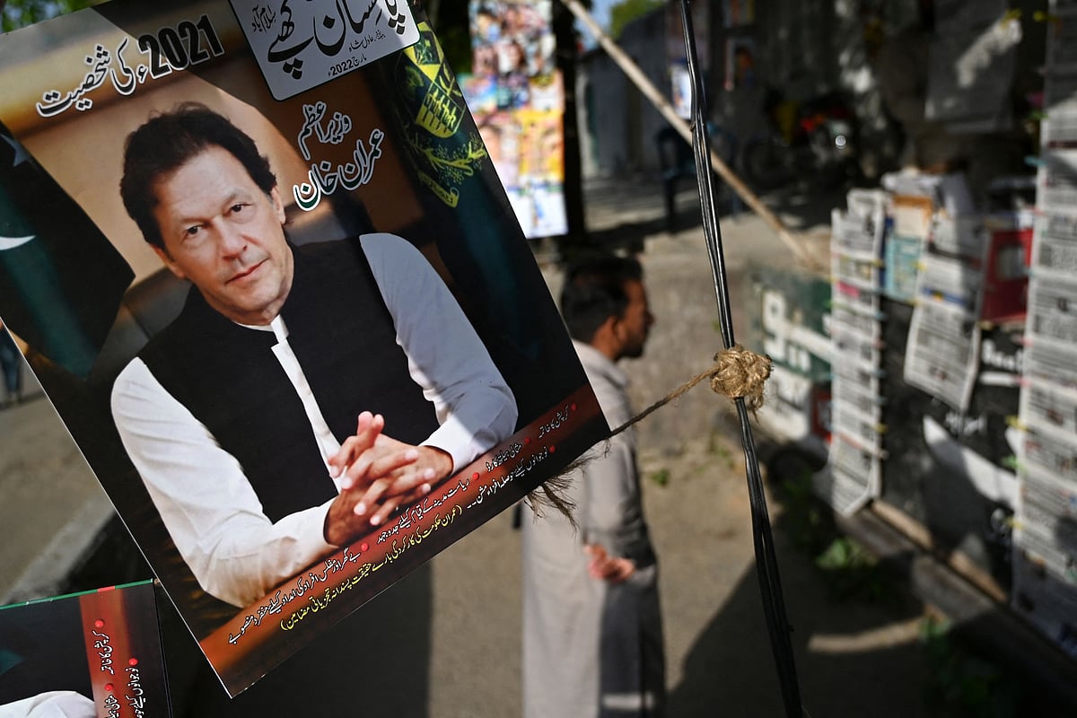 A resident stands beside a picture of Pakistan's Prime Minister Imran Khan as he looks at the morning newspapers displayed for sale at a roadside stall in Islamabad on 4 April 2022, a day after Khan foiled an attempt to boot him from office by getting the president to dissolve the national assembly, meaning fresh elections must be held within three months.