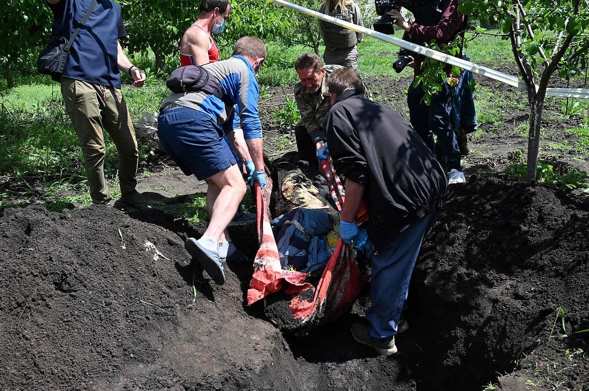 Local residents assist a Ukrainian police forensic team to exhume the body of a 51-year-old man allegedly shot dead on March 25, 2022 by a Russian soldier in the courtyard of his house, in the village of Mala Rogan, near Kharkiv on 23 May, 2022