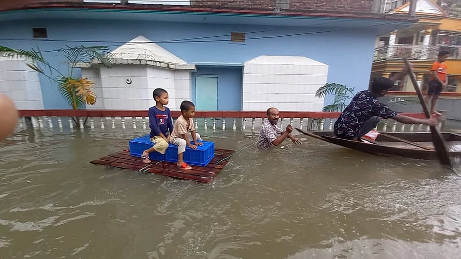 Two children sit on a raft made of wood and plastic crates as a man pulls the raft wading through chest-deep water on a road in Sunamgaj city on 19 June 2022