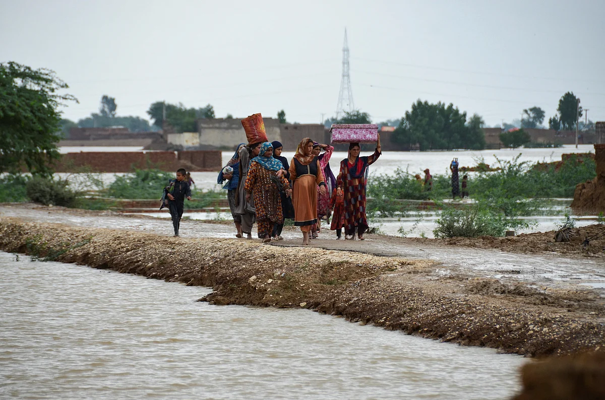 Women and children walk with their belongings towards a higher ground following rains and floods during the monsoon season in Dera Allah Yar, district Jafferabad, Balochistan, Pakistan on 25 August, 2022