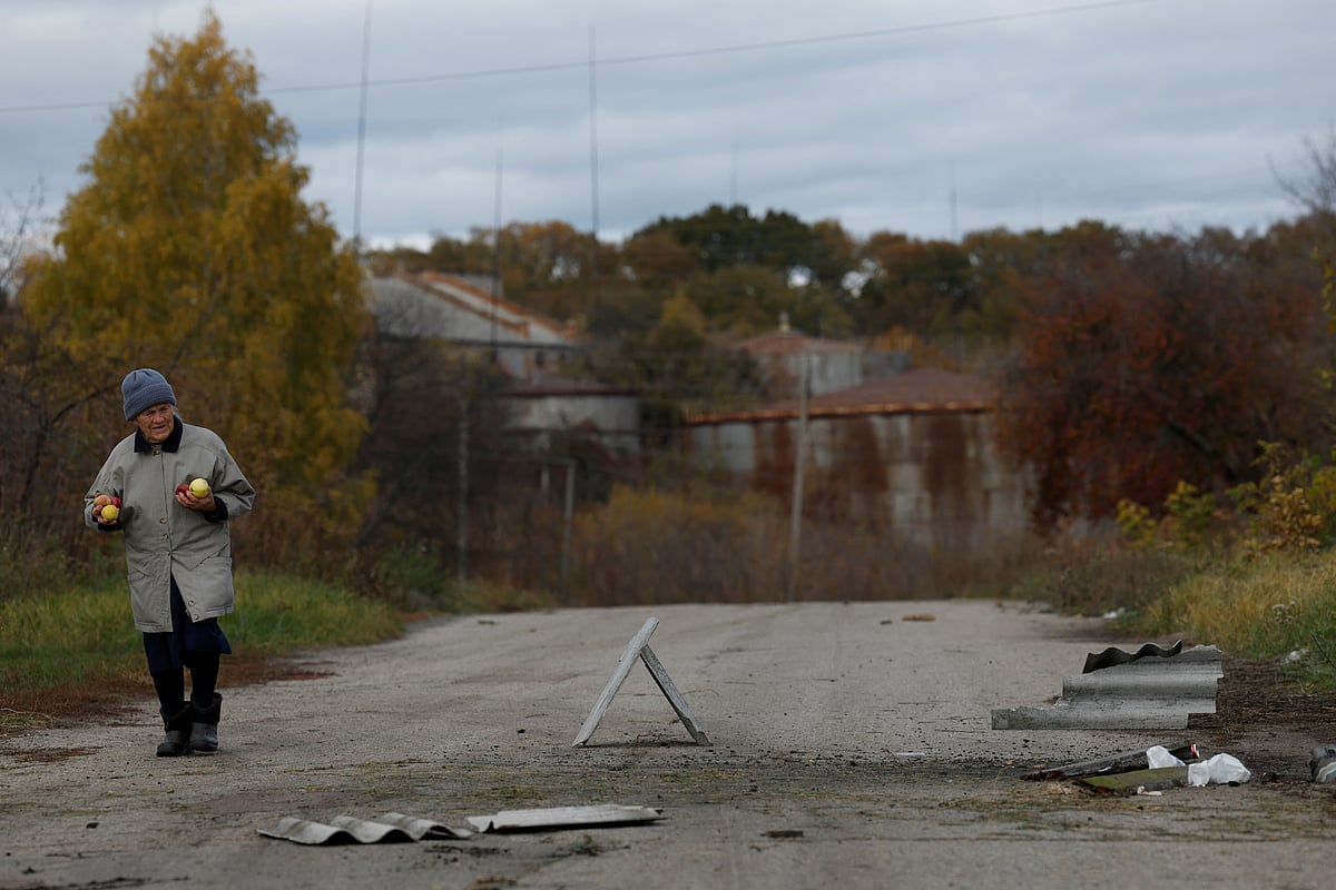 A woman carries apples walks past the site of a missile strike, amid Russia’s attack on Ukraine, near the Russian border in Kharkiv region, Ukraine, on 21 October, 2022