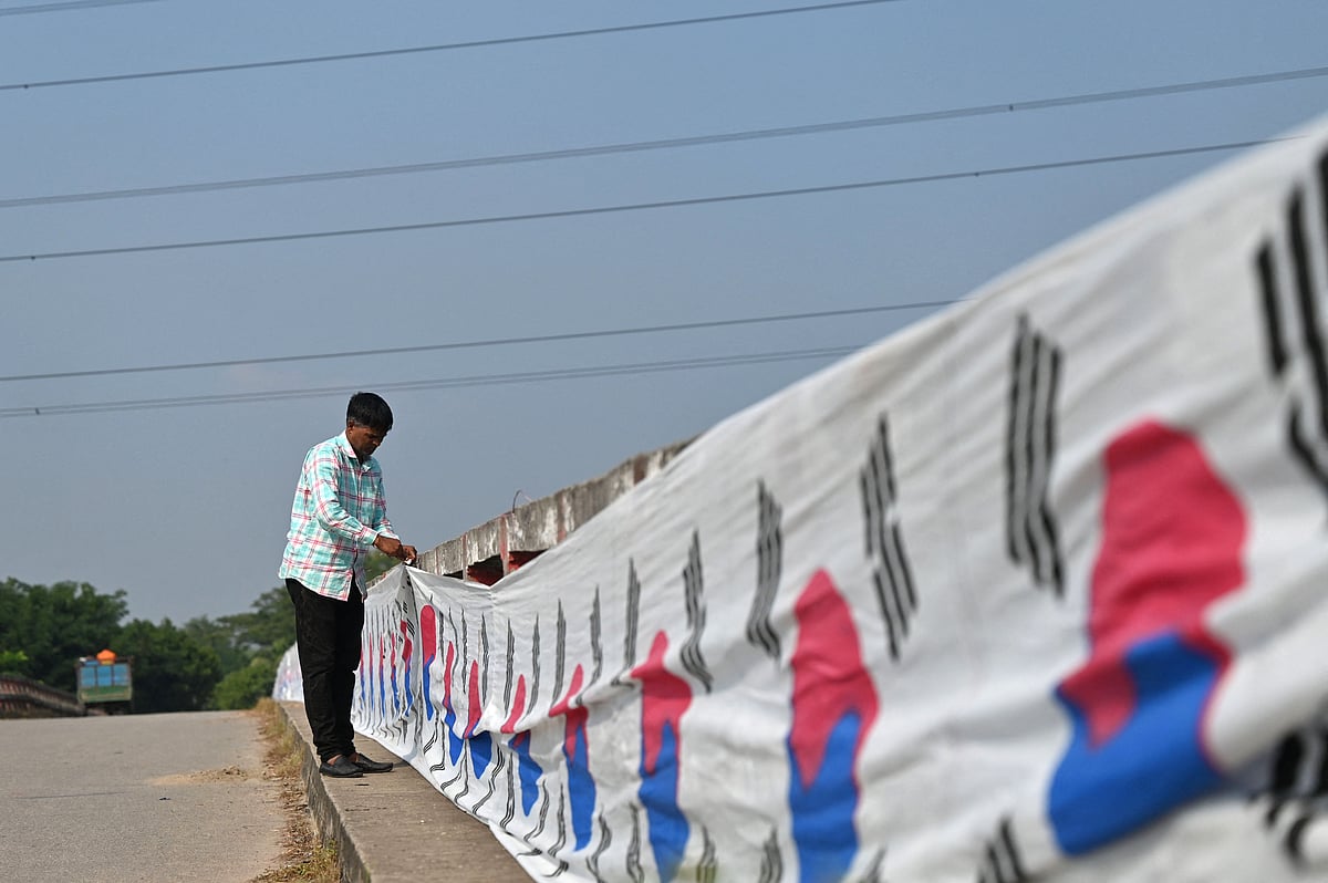 In this photograph taken on 16 November, 2022, Bangladeshi chemist Abu Kowsir, who is a South Korea football fan, puts up a 3.5-kilometre long (2.2 mile-long) flag of South Korea along a bridge from his home to a neighbouring village