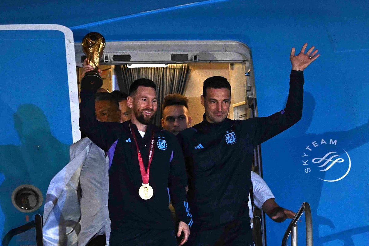 Argentina's captain and forward Lionel Messi (L) holds the FIFA World Cup Trophy alongside Argentina's coach Lionel Scaloni as they step off a plane upon arrival at Ezeiza International Airport after winning the Qatar 2022 World Cup tournament in Ezeiza, Buenos Aires province, Argentina on 20 December, 2022
