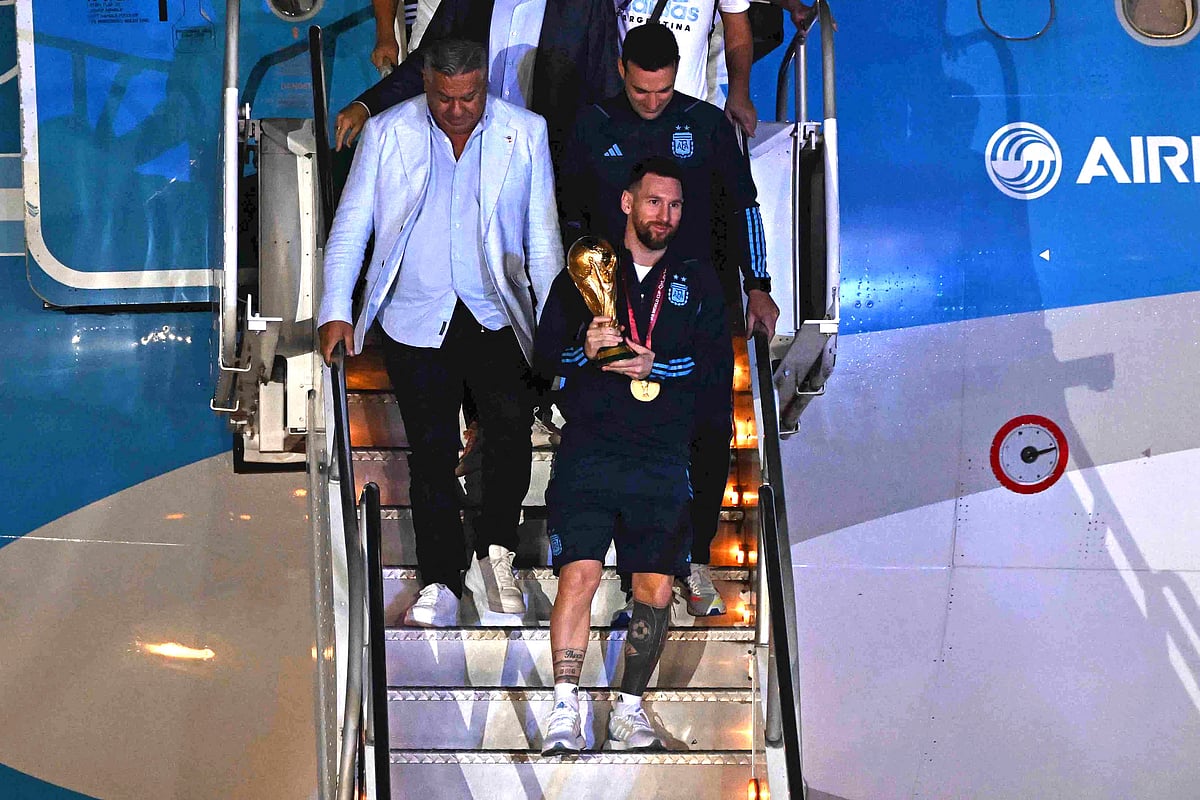Argentina's captain and forward Lionel Messi (C) holds the FIFA World Cup Trophy as he steps off a plane upon arrival at Ezeiza International Airport after winning the Qatar 2022 World Cup tournament in Ezeiza, Buenos Aires province, Argentina on December 20, 2022