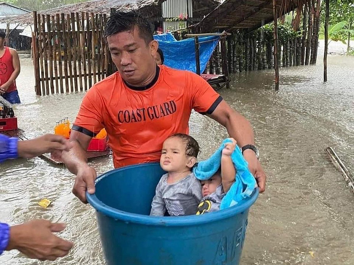 This handout photo taken and released by the Philippine Coast Guard on 11 January, 2023 shows rescue workers evacuating children from a flooded area in Zamboanga.
