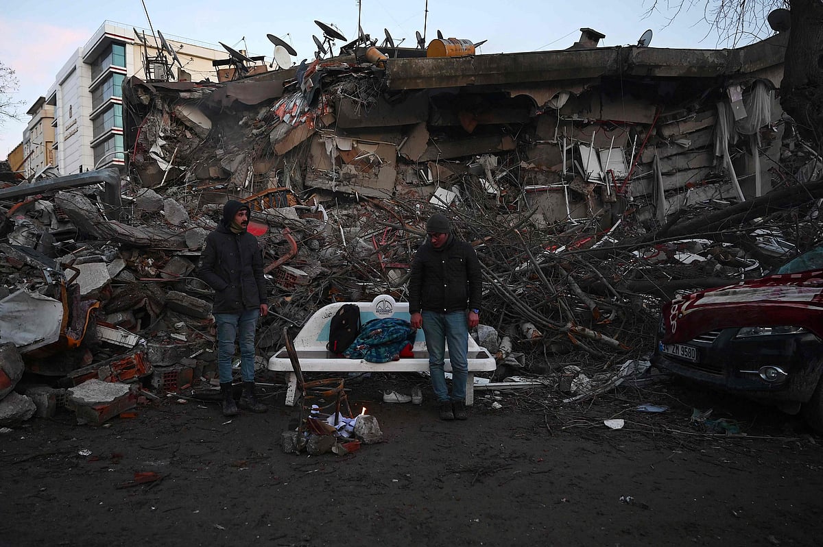 People light a bonfire amid the rubble of collapsed buildings in Kahramanmaras, on 7 February, 2023