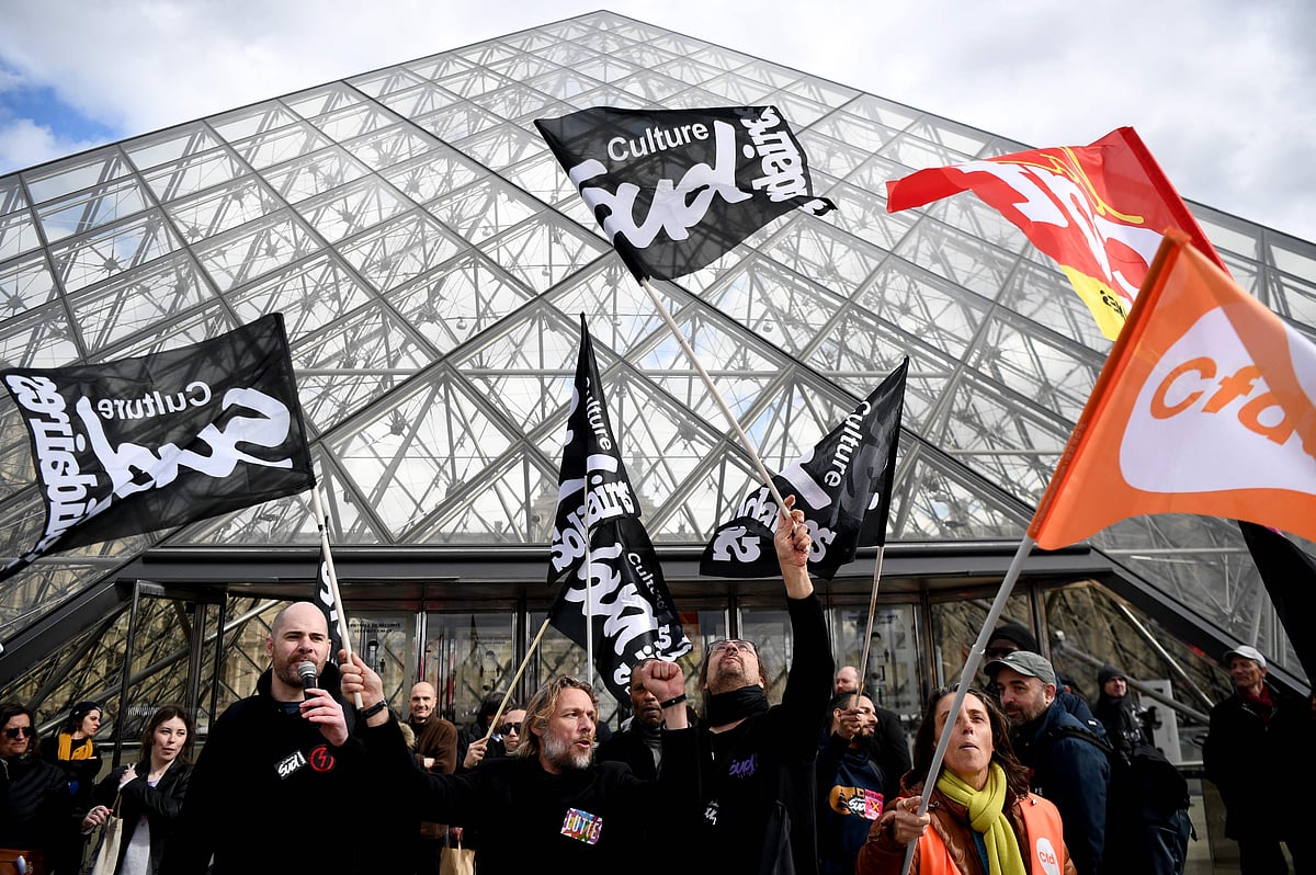 Employees hold banners and unions' flags as they block the entrance of the Musee du Louvre to denounce government's controversial pension reform, in Paris, on 27 March, 2023