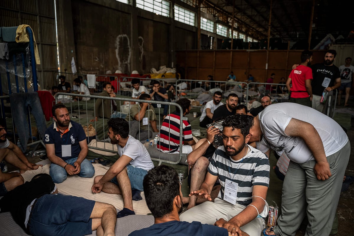 Survivors of a shipwreck sit inside a warehouse at the port in Kalamata town, on 15 June, 2023, after a boat carrying migrants sank in international waters in the Ionian Sea