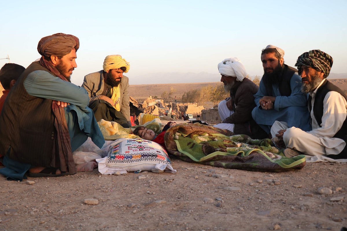 Afghan men sit by the bodies of relatives killed after an earthquake in Sarbuland village of Zendeh Jan district of Herat province on October 7,2023