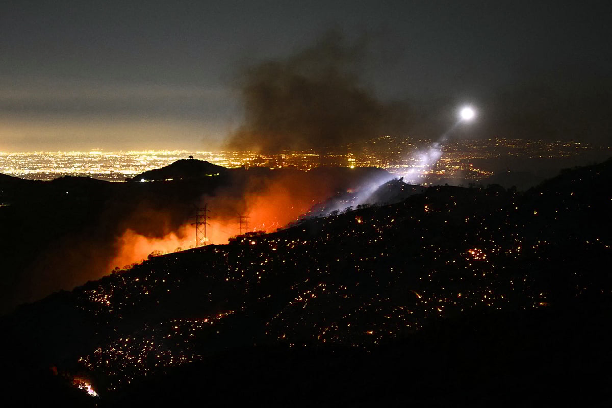 The light of a fire fighting helicopter illuminates a smouldering hillside as the Palisades fire grows near the Mandeville Canyon neighborhood and Encino, California, on 11 January, 2025. The Palisades Fire, the largest of the Los Angeles fires, spread toward previously untouched neighborhoods 11 January, forcing new evacuations and dimming hopes that the disaster was coming under control.