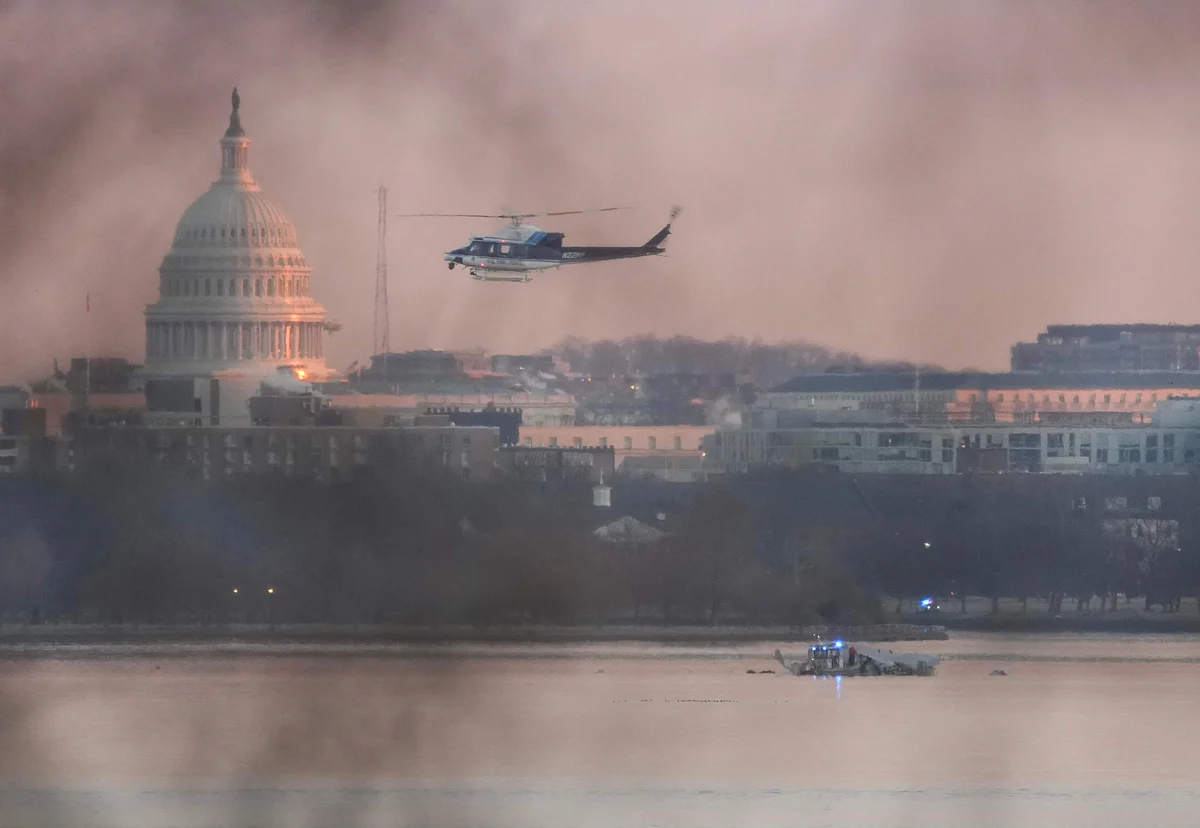 A helicopter flies near the crash site of the American Airlines plane on the Potomac River after the plane crashed on approach to Reagan National Airport on January 30, 2025 in Arlington, Virginia.