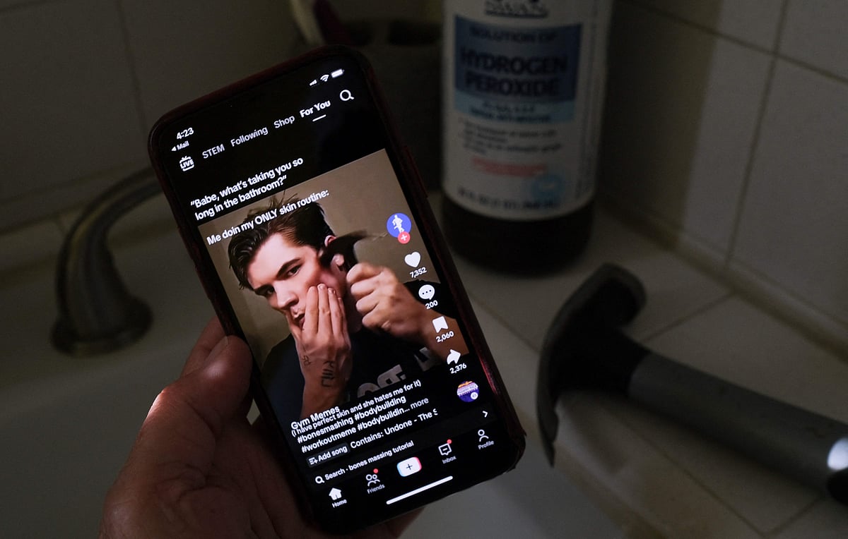 This illustration photo shows a video of male TikTok influencer hammering his cheekbone, playing on a smartphone in a bathroom next to a bottle of hydrogen peroxide and a hammer in Los Angeles, 11 April 2025.